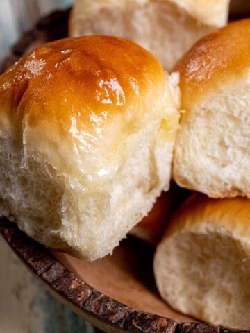 A wooden serving bowl full of honey butter yeast rolls with honey buttered tops.
