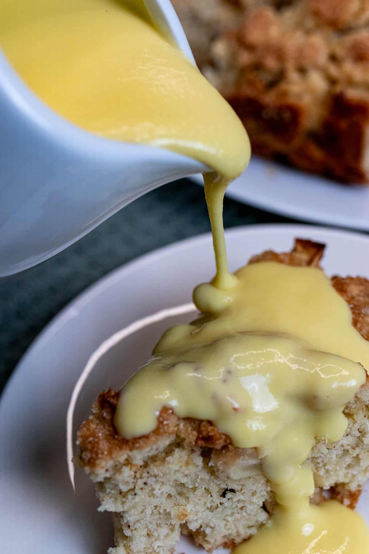 Pouring vanilla custard sauce over a slice of Irish apple cake.