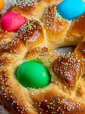 Italian Easter bread braided and shaped into a wreath, decorated with colored eggs and pastel sprinkles.