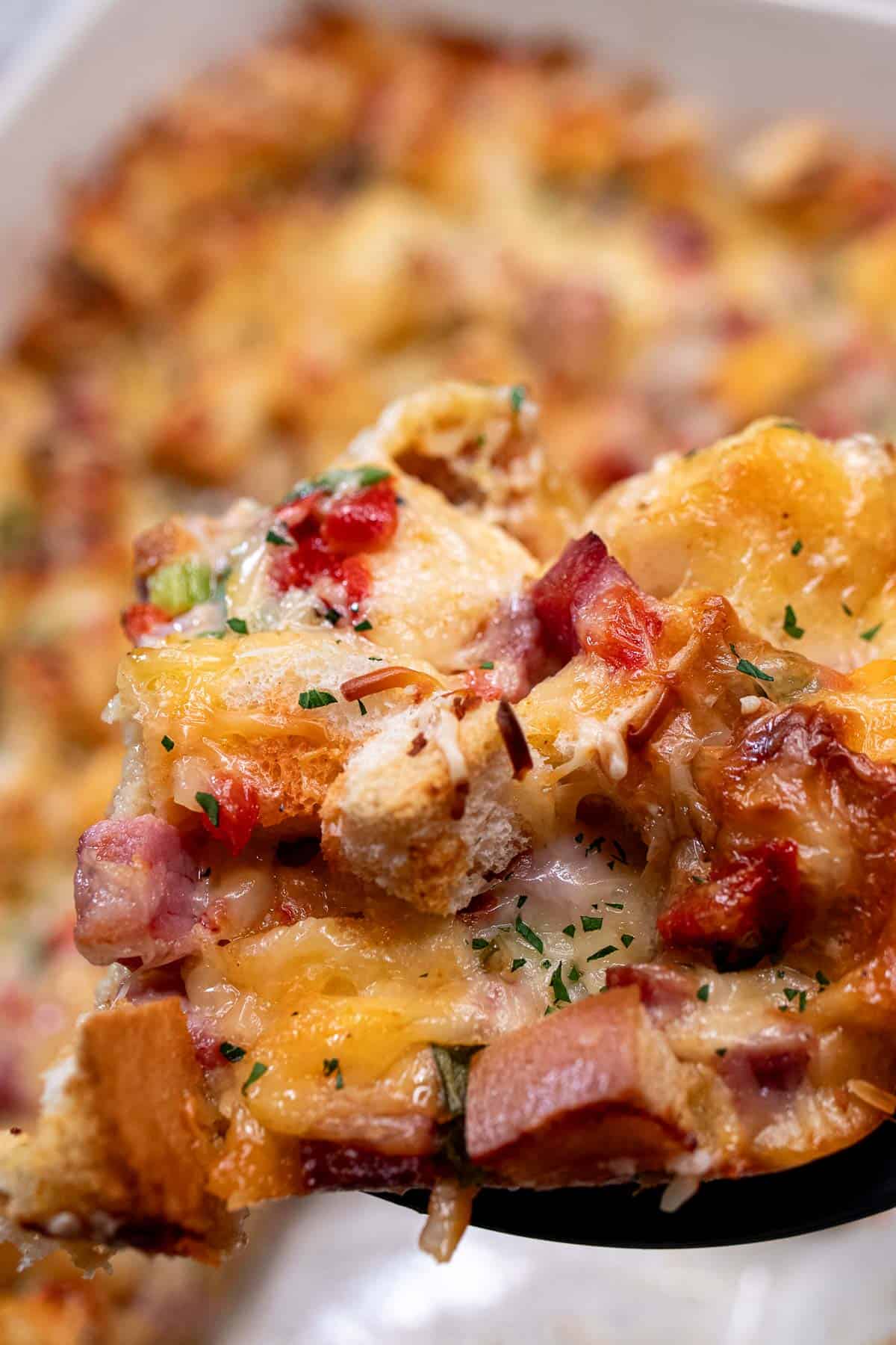 A portion of ham and cheese strata being scooped out of the baking dish.