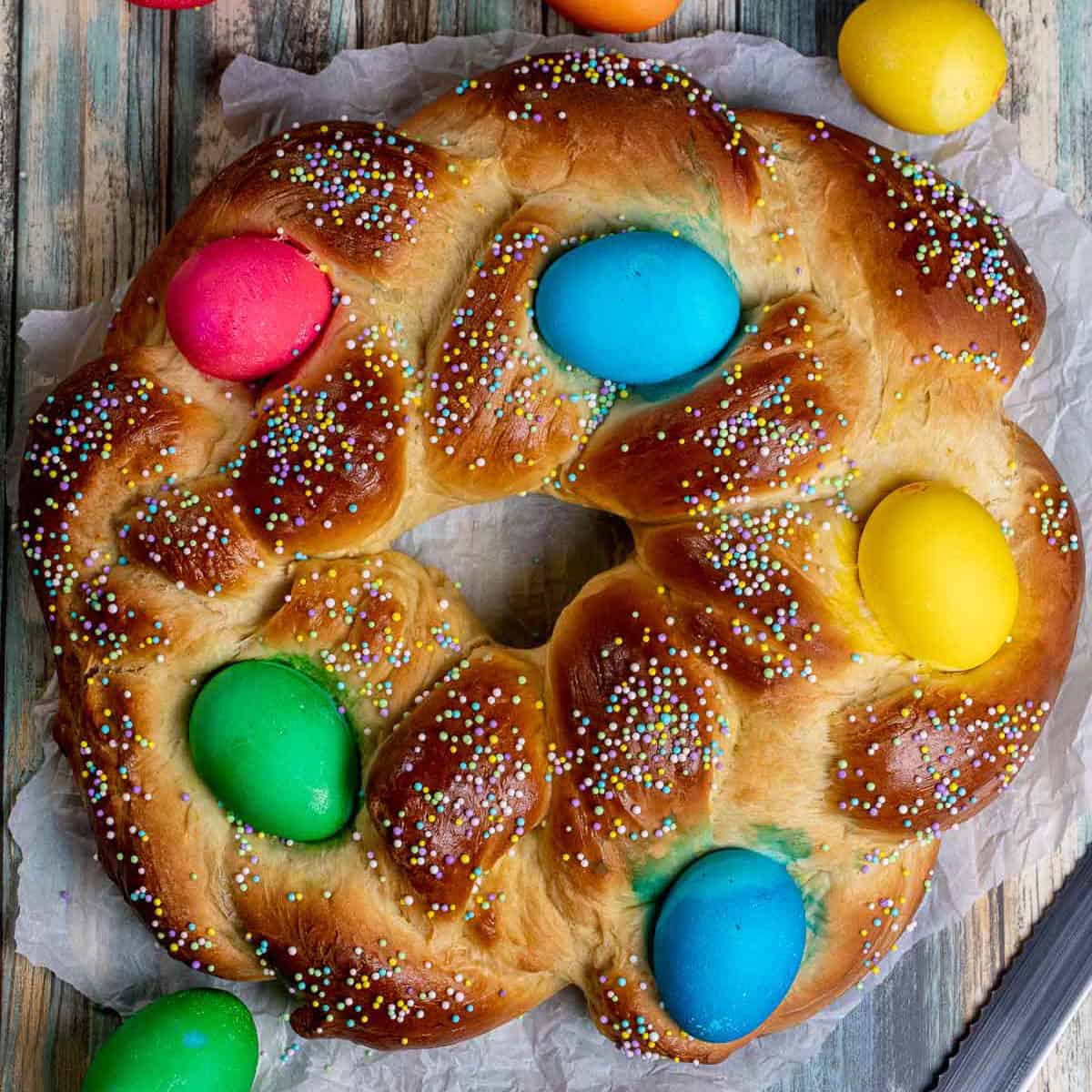Baked and cooled braided pani di Pasqua with dyed eggs on and around it.