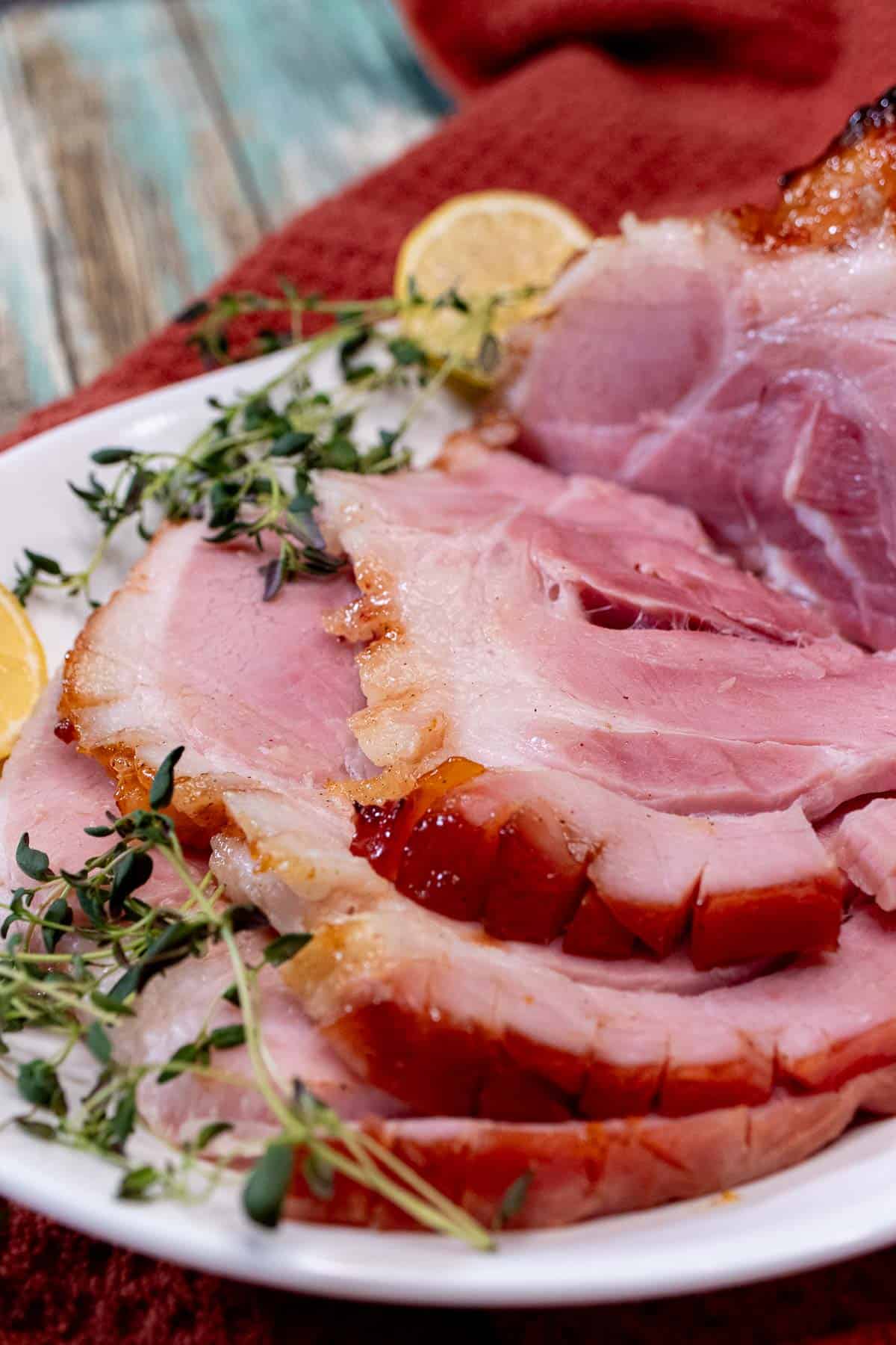 A carved peach and bourbon glazed ham on a platter with fresh thyme and lemon.