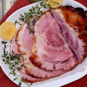 A partially carved peach and bourbon glazed baked ham on a serving platter.