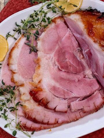 A partially carved peach and bourbon glazed baked ham on a serving platter.