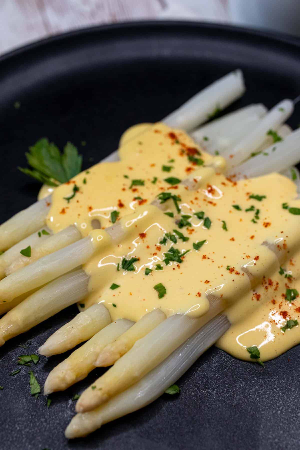 White asparagus on a serving plate, topped with hollandaise sauce and fresh parsley.