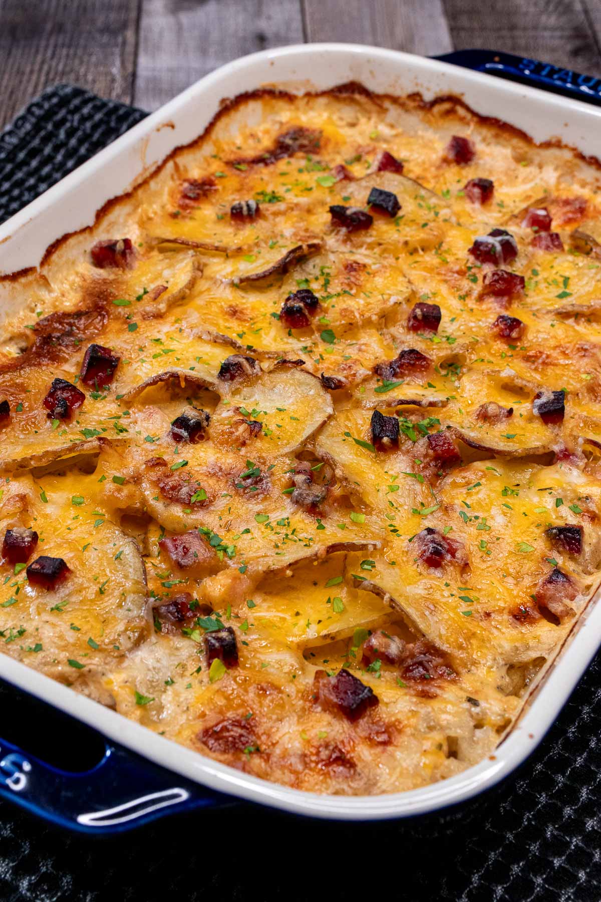 An enameled baking dish filled with scalloped potatoes studded with ham and topped with cheese.