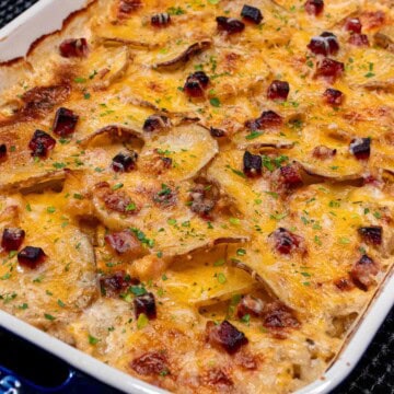 A baking dish full of cheesy scalloped potatoes and ham.