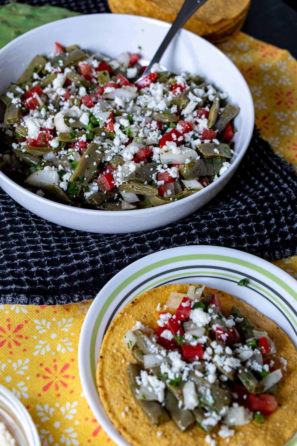 A large bowl of ensalada de nopales, with a portion served on top of a tostado.