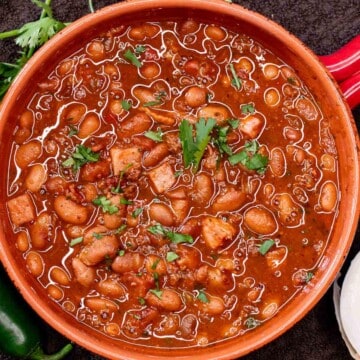 A serving bowl filled with Mexican charro beans, topped with fresh cilantro.