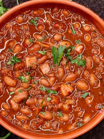 A serving bowl filled with Mexican charro beans, topped with fresh cilantro.