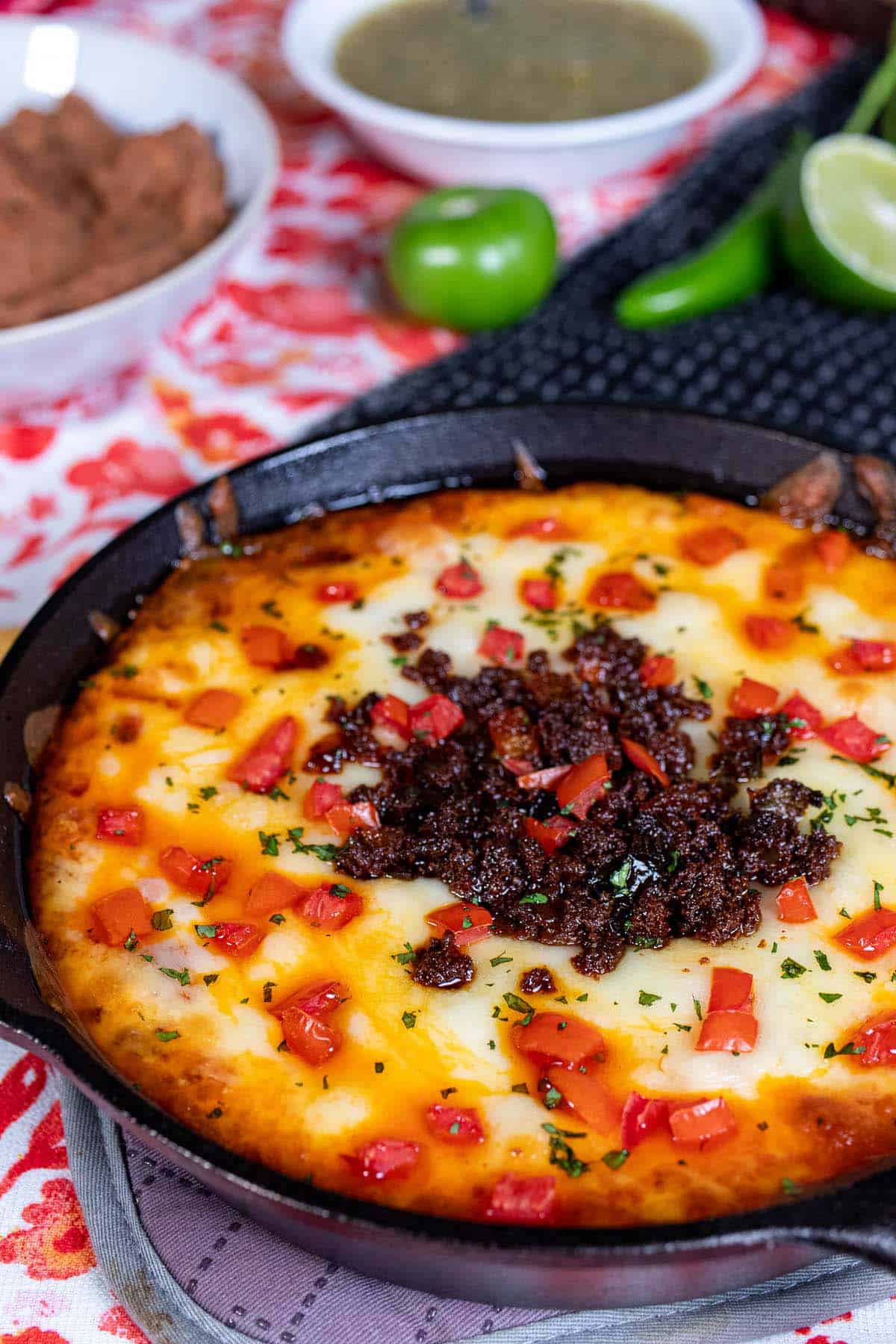 A skillet of queso fundido topped with chorizo, tomato, and cilantro.