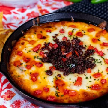 Queso fundido in a cast iron skillet topped with chorizo, diced tomato, and fresh cilantro.