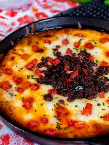Queso fundido in a cast iron skillet topped with chorizo, diced tomato, and fresh cilantro.