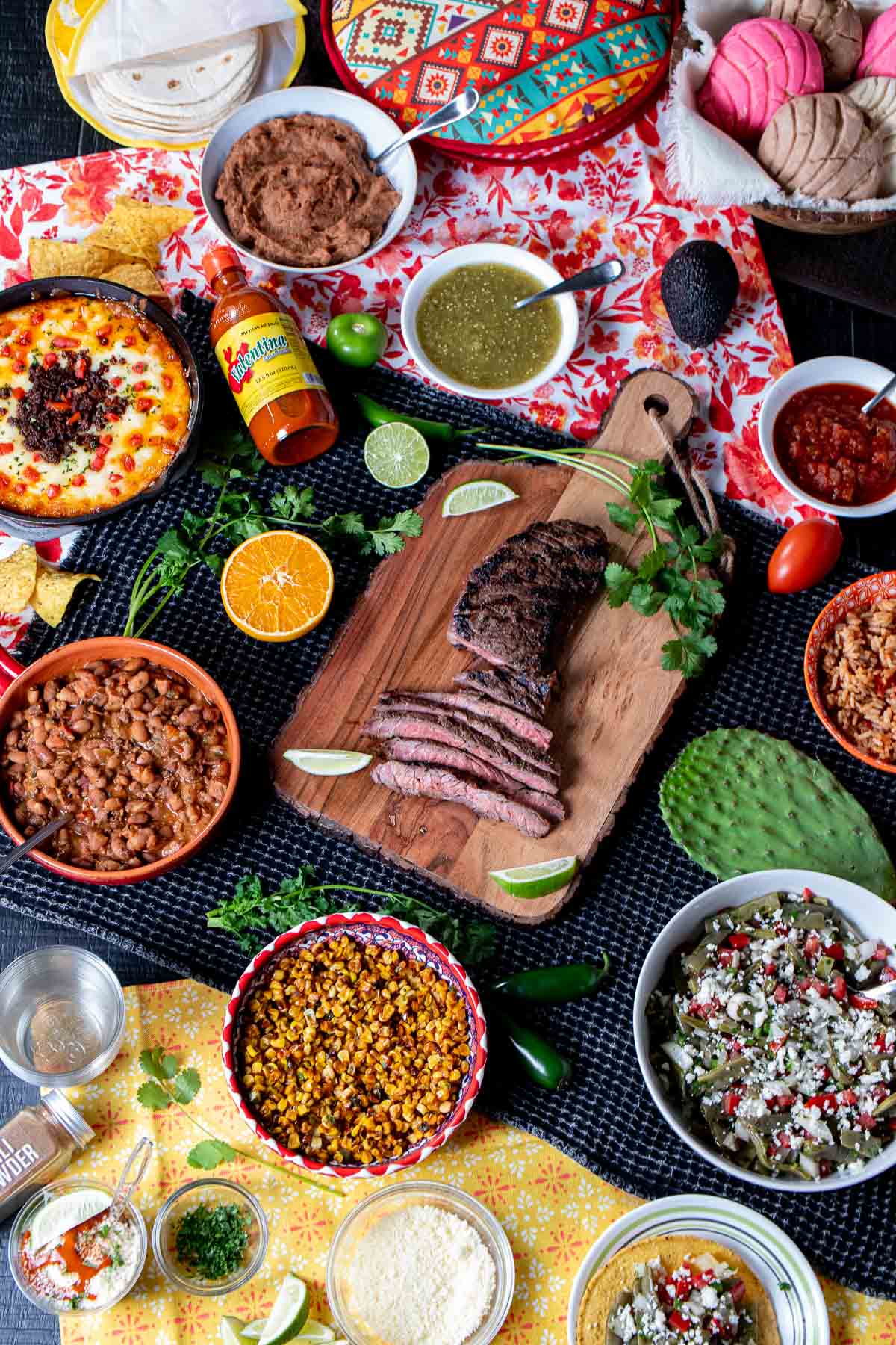 Carne asada steak as the centerpiece of a meal with lots of sides of beans, rice, salad, salsas and others.