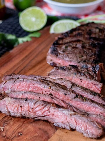 A sliced carne asada skirt steak on a wooden board, with cut limes and orange around it.