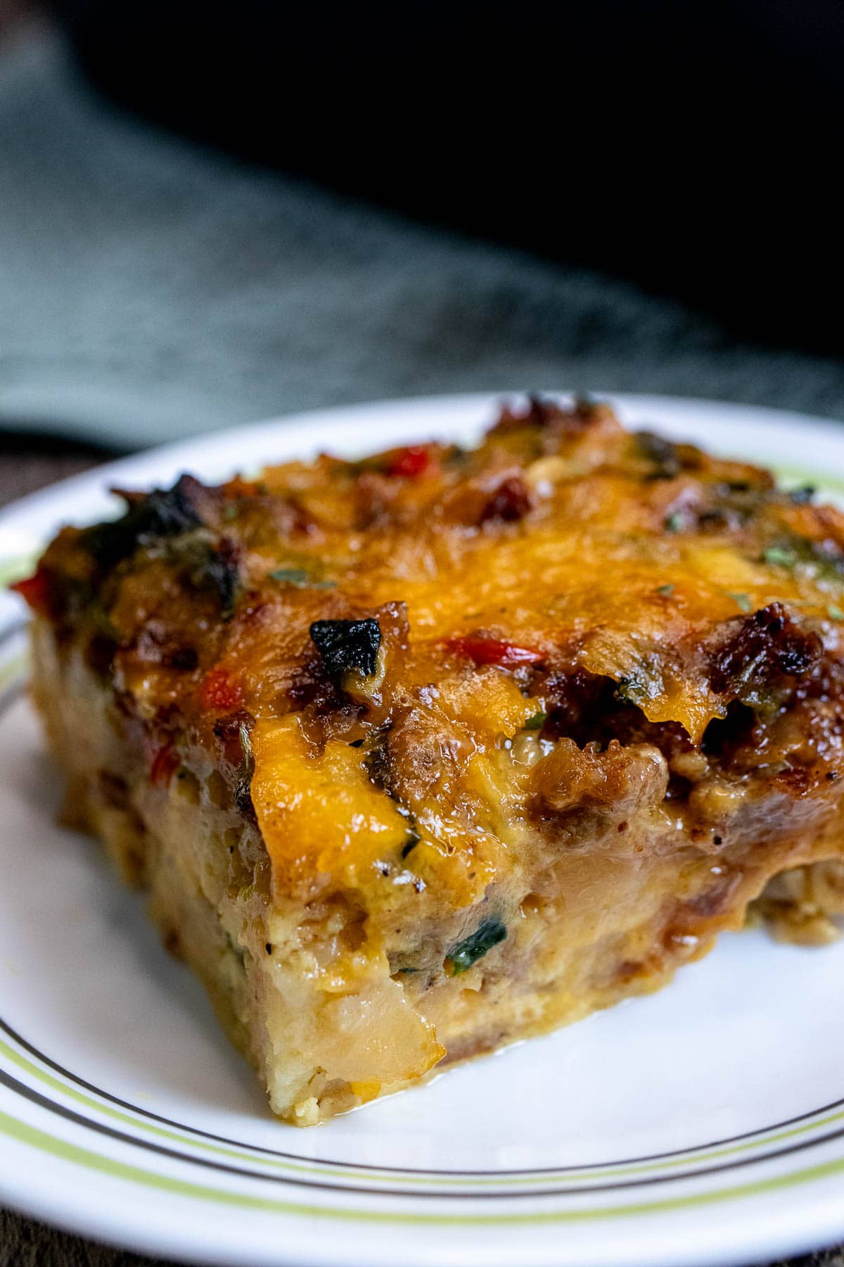 A large slice of breakfast casserole with sausage, onion, peppers, spinach, and cheese on a plate.