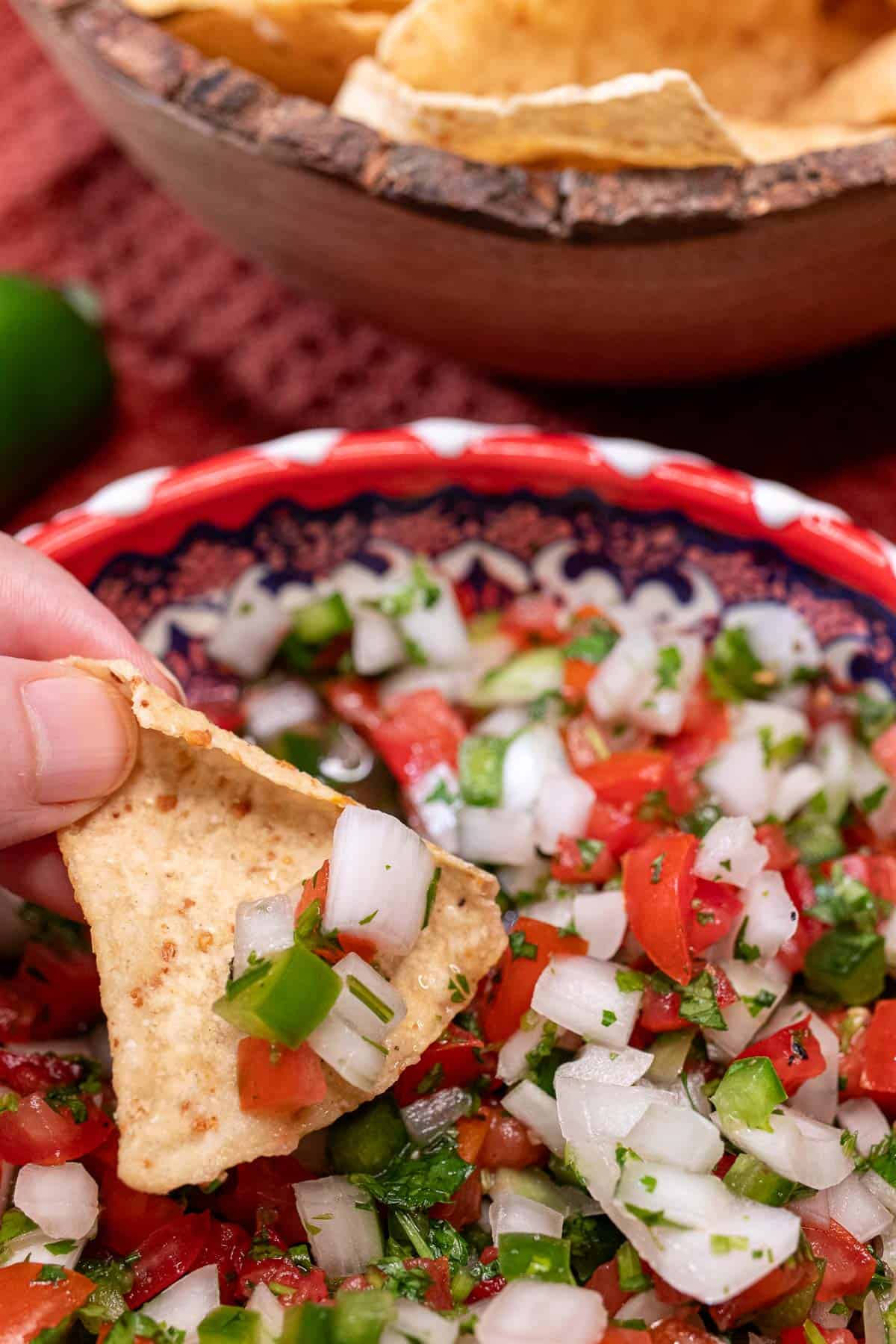Classic pico de gallo being scooped from a bowl with a tortilla chip.