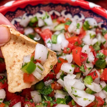 A bowl of fresh, classic pico de gallo being scooped up with a tortilla chip.