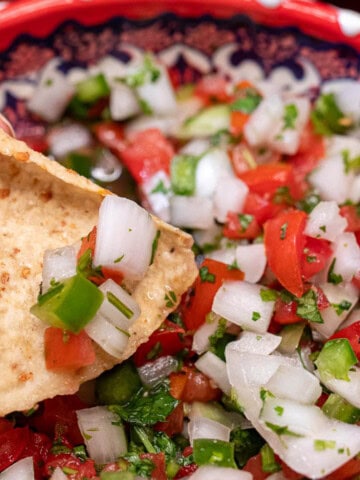 A bowl of fresh, classic pico de gallo being scooped up with a tortilla chip.