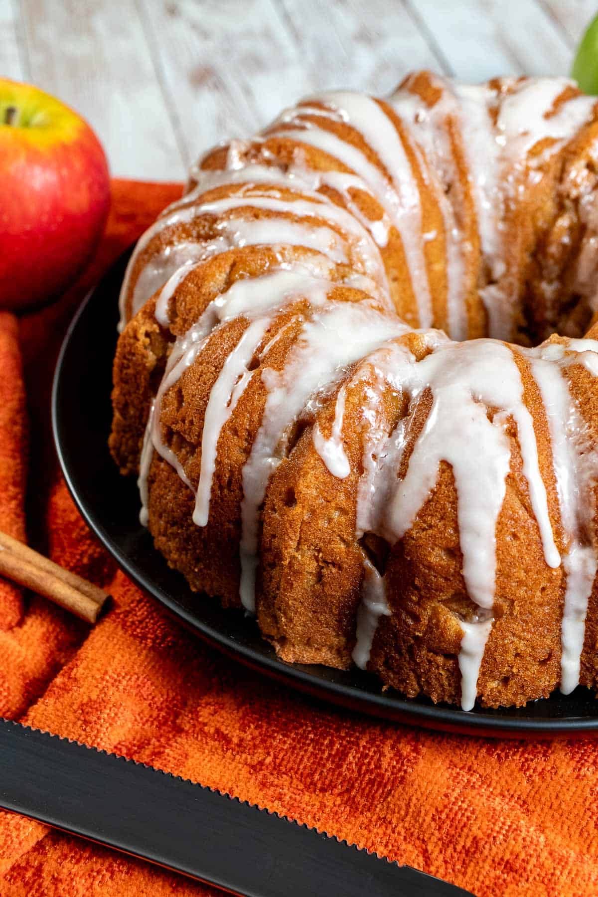 An unsliced cider glazed apple Bundt cake with an apple and cinnamon stick next to it.