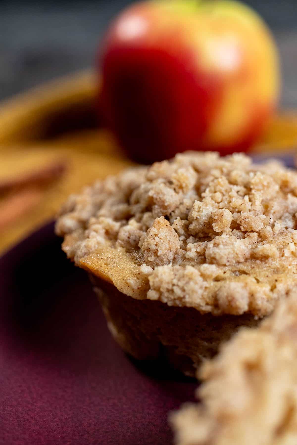 A cinnamon apple muffin with an apple and cinnamon sticks in the background.