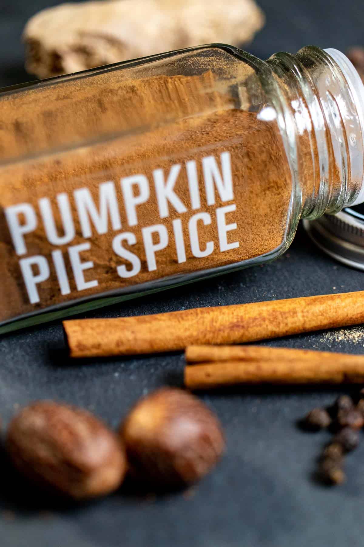 A small spice jar labeled and filled with homemade pumpkin pie spice with whole spices around it.