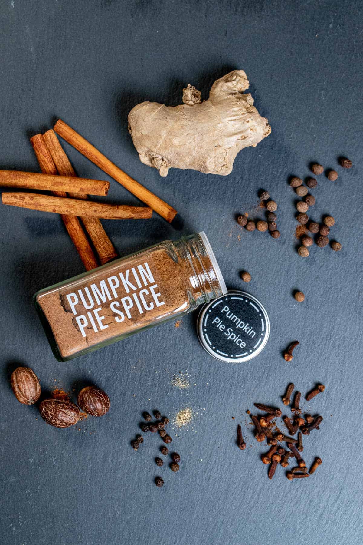 A jar of pumpkin pie spice with the whole spice ingredients laying around it.