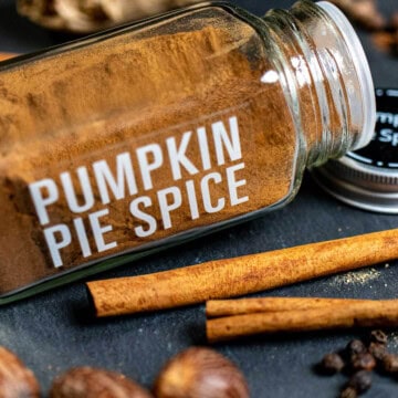 A spice jar filled with homemade pumpkin pie spice with whole spices around it.