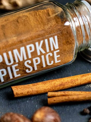 A spice jar filled with homemade pumpkin pie spice with whole spices around it.