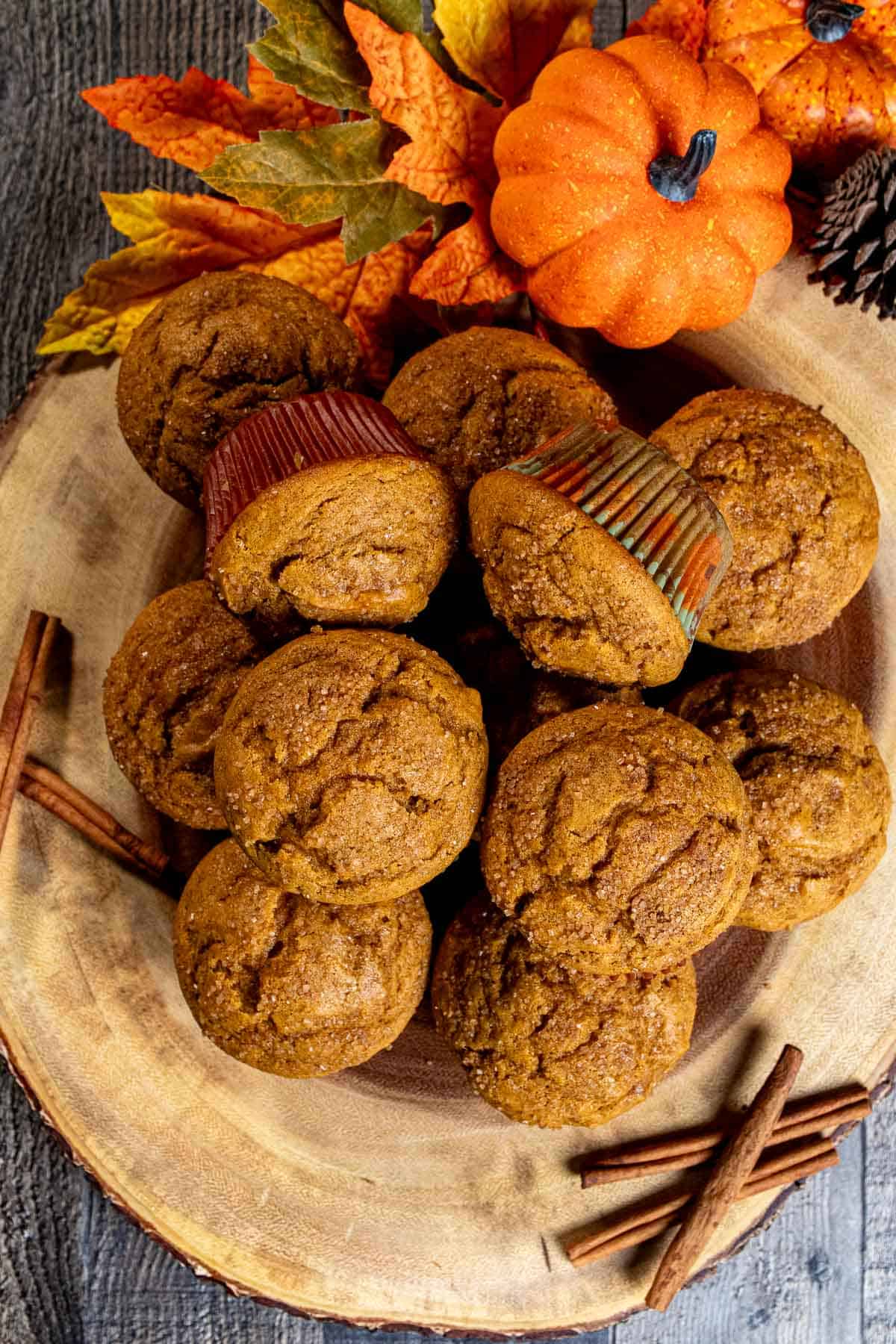 A pile of pumpkin spice muffins on a wooden board with pumpkins and cinnamon sticks around them.