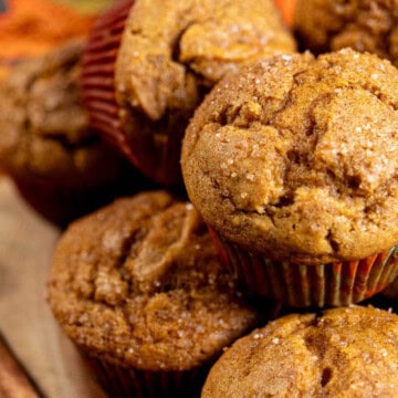 Pumpkin spice muffins stacked on top of each other with a cinnamon stick next to them.