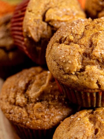 Pumpkin spice muffins stacked on top of each other with a cinnamon stick next to them.