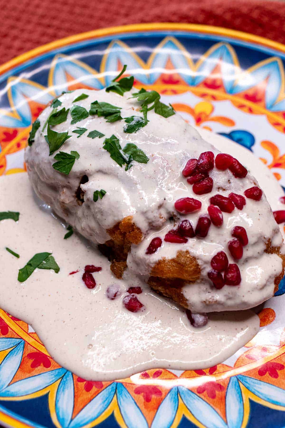 A sweet and savory stuffed poblano covered in a walnut sauce on a festive plate.