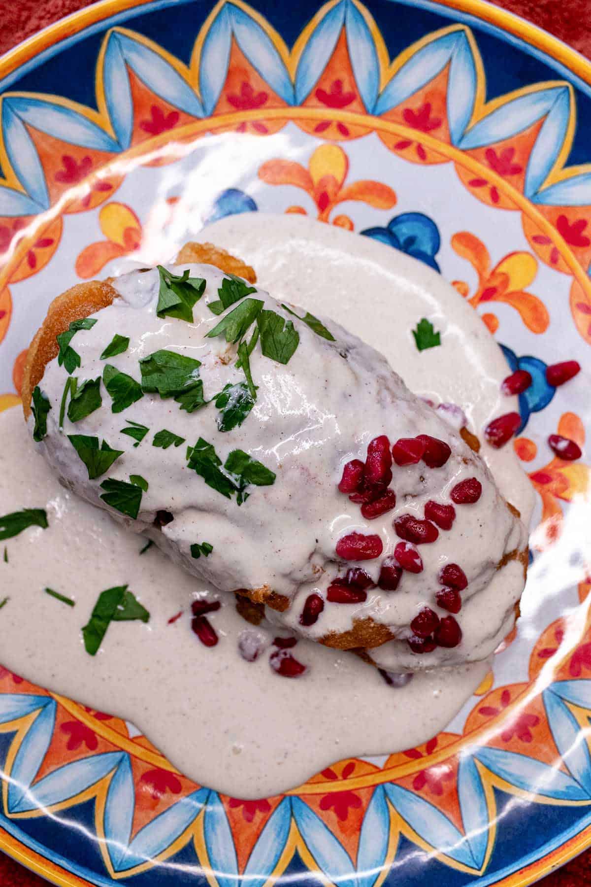 A picadillo stuffed and fried poblano pepper plated and covered in a walnut sauce and topped with parsley and pomegranate seeds for chiles en nogada.