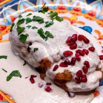 A chile en nogada on a festive Mexican plate, topped with parsley and pomegranate seeds.