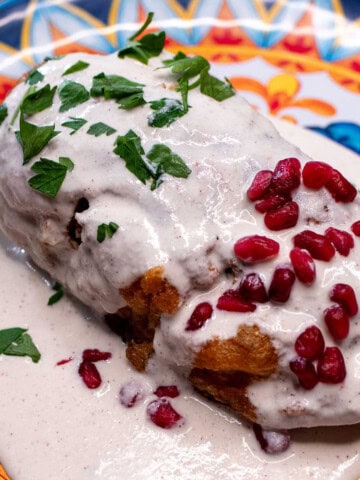 A chile en nogada on a festive Mexican plate, topped with parsley and pomegranate seeds.