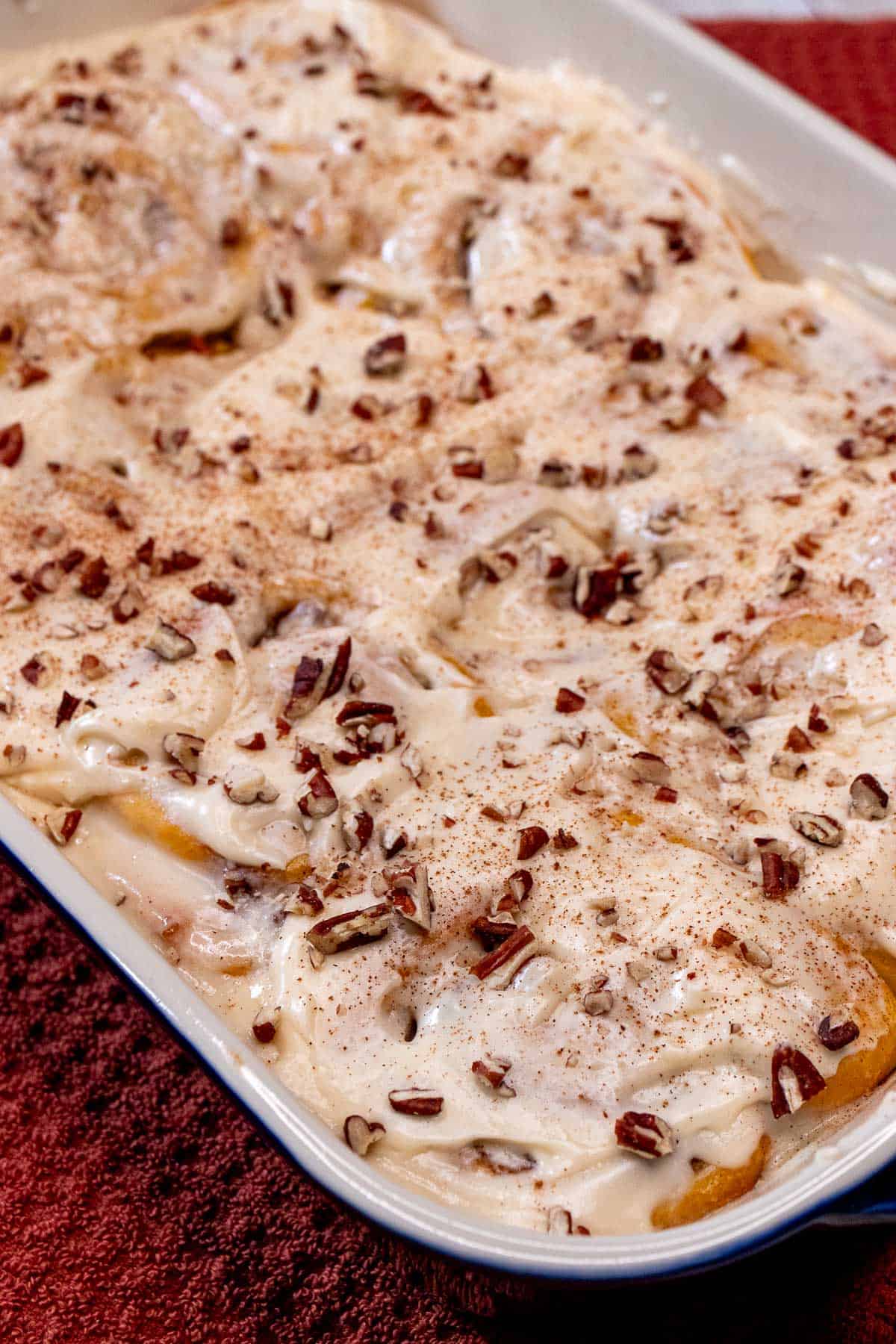A baking dish full of frosted pumpkin pecan cinnamon rolls.