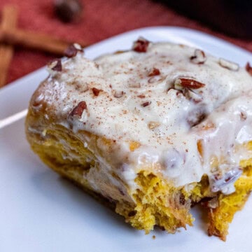 Maple cream cheese frosted pumpkin pecan cinnamon roll on a plate.