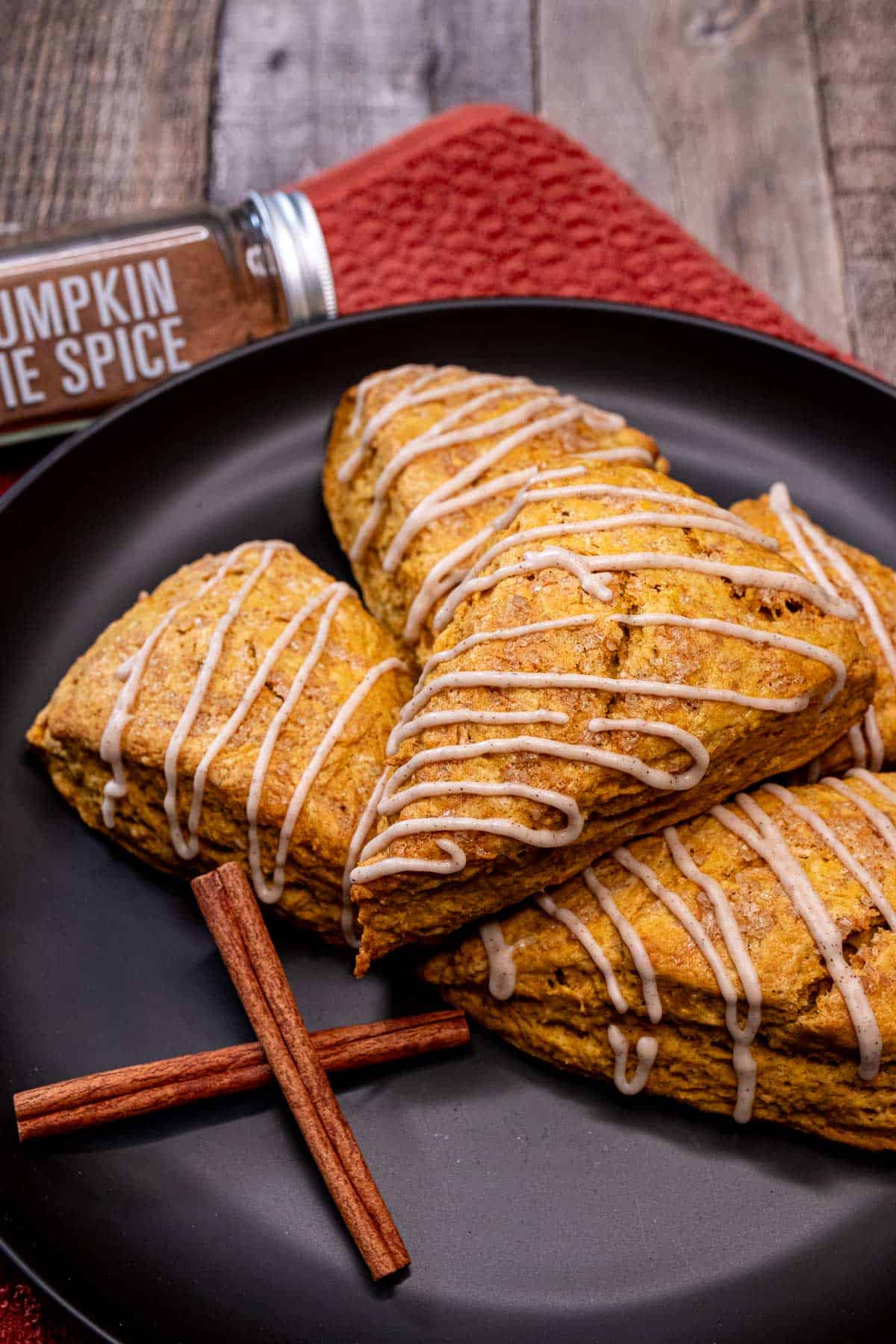 Pumpkin scones on a plate with cinnamon sticks and a jar of pumpkin pie spice behind them.