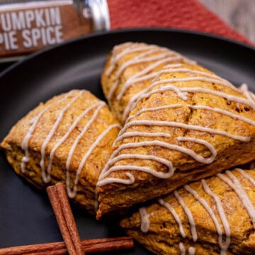A plate full of pumpkin scones with a maple cinnamon glaze drizzled over them.