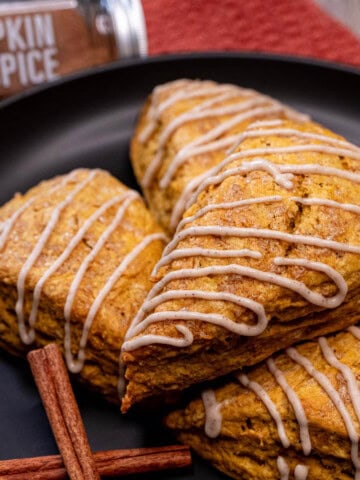 A plate full of pumpkin scones with a maple cinnamon glaze drizzled over them.